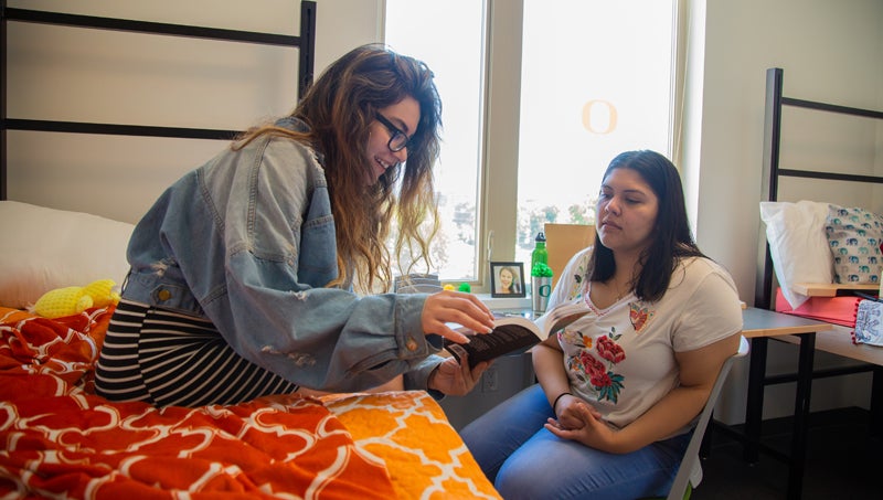 Two students in residence hall room reading a book.