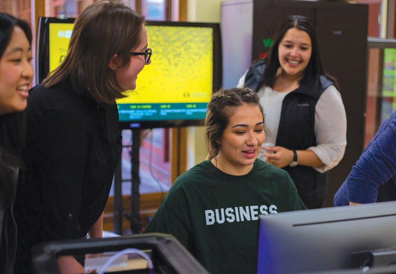 Students gathered around computer conversing about business