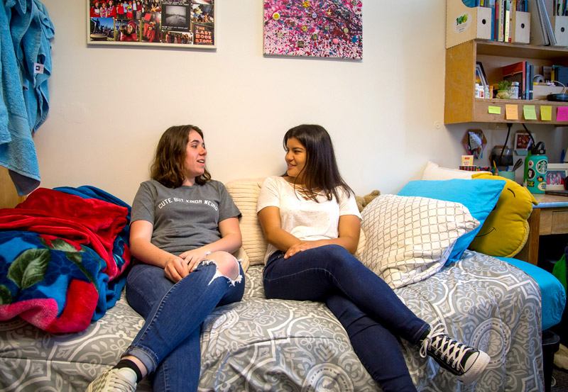 Photo of two students conversing on bed.